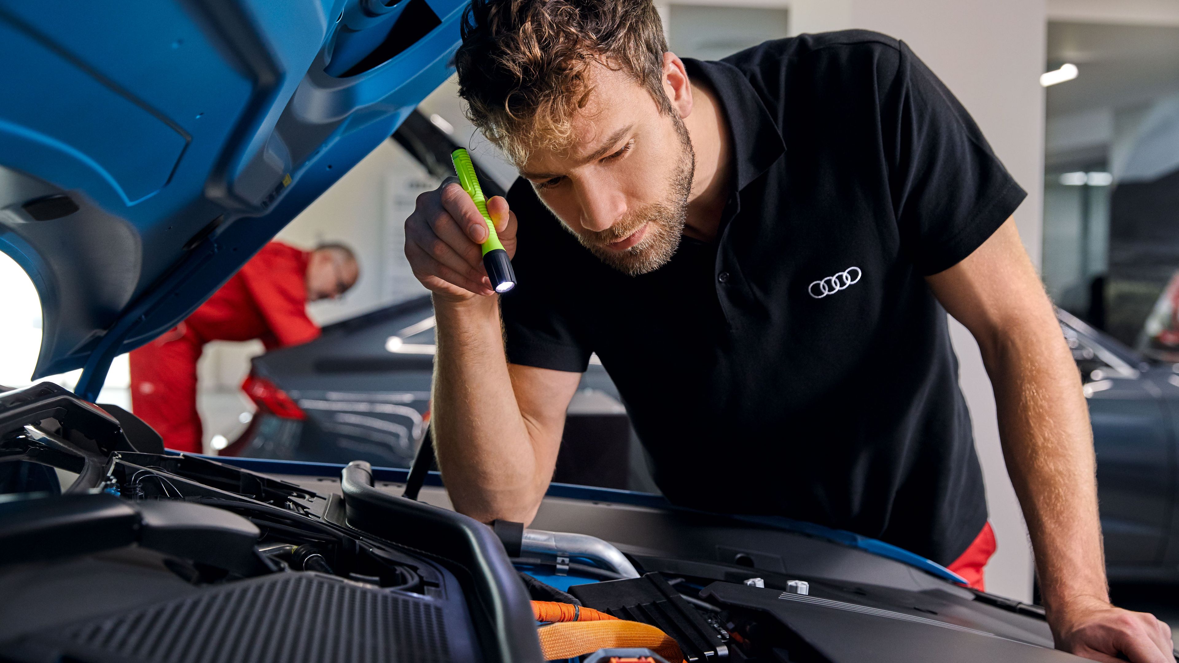 Ein Audi Service Techniker leuchtet mit einer Taschenlampe in den Motorraum eines Audi