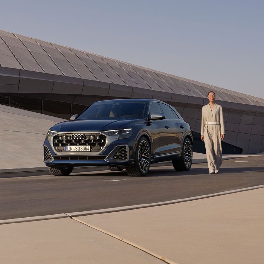 Модерен сив SUV Audi е паркиран на широк, гладък път пред 