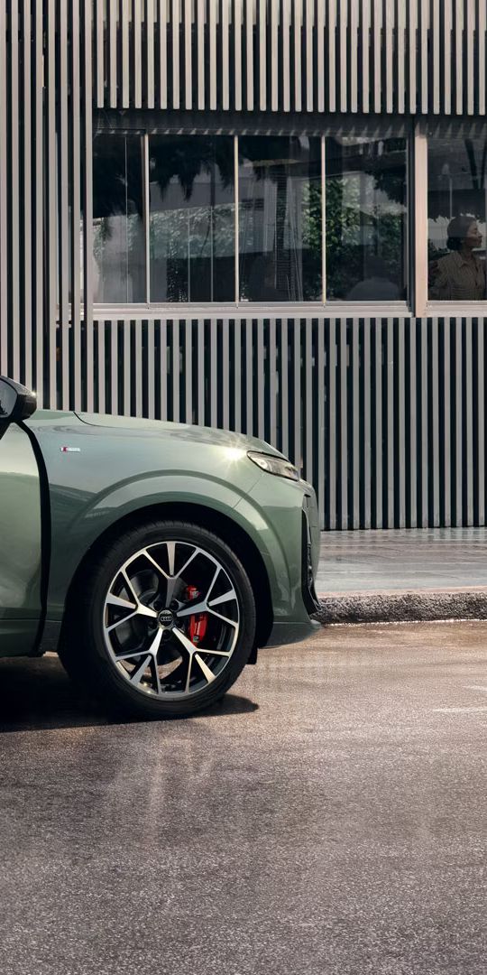 Ein Mann steht an der offenen Beifahrertür eines Audi Q3 SUV, der vor einem Gebäude parkt.