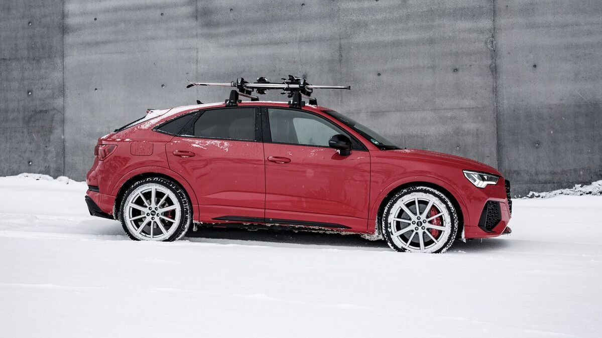 Mann steht mit seinem Audi und Ski inmitten von Bergen