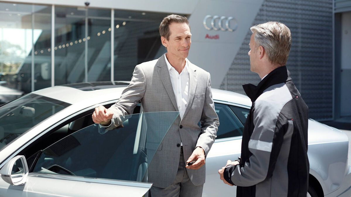 Ein Audi Service Mitarbeiter im Kundengespräch, der Kunde hält die Türe seines Audi offen