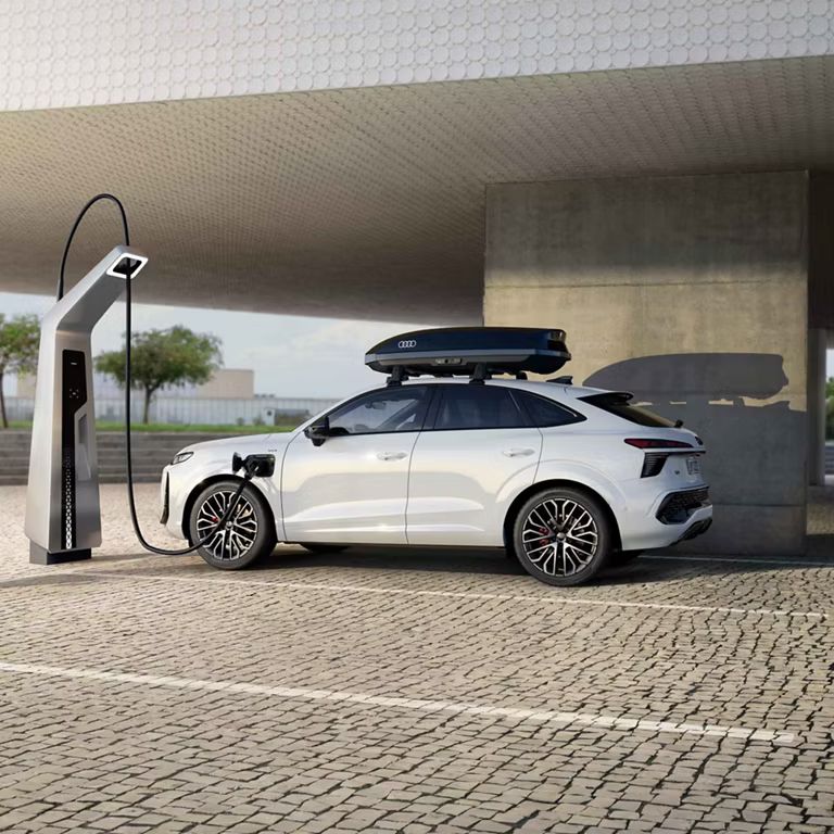 Der Audi Q3 SUV Sportback von der Seite auf einem Parkplatz beim Laden. Weiterhin ist eine Dachbox auf dem weißen Auto zu erkennen.