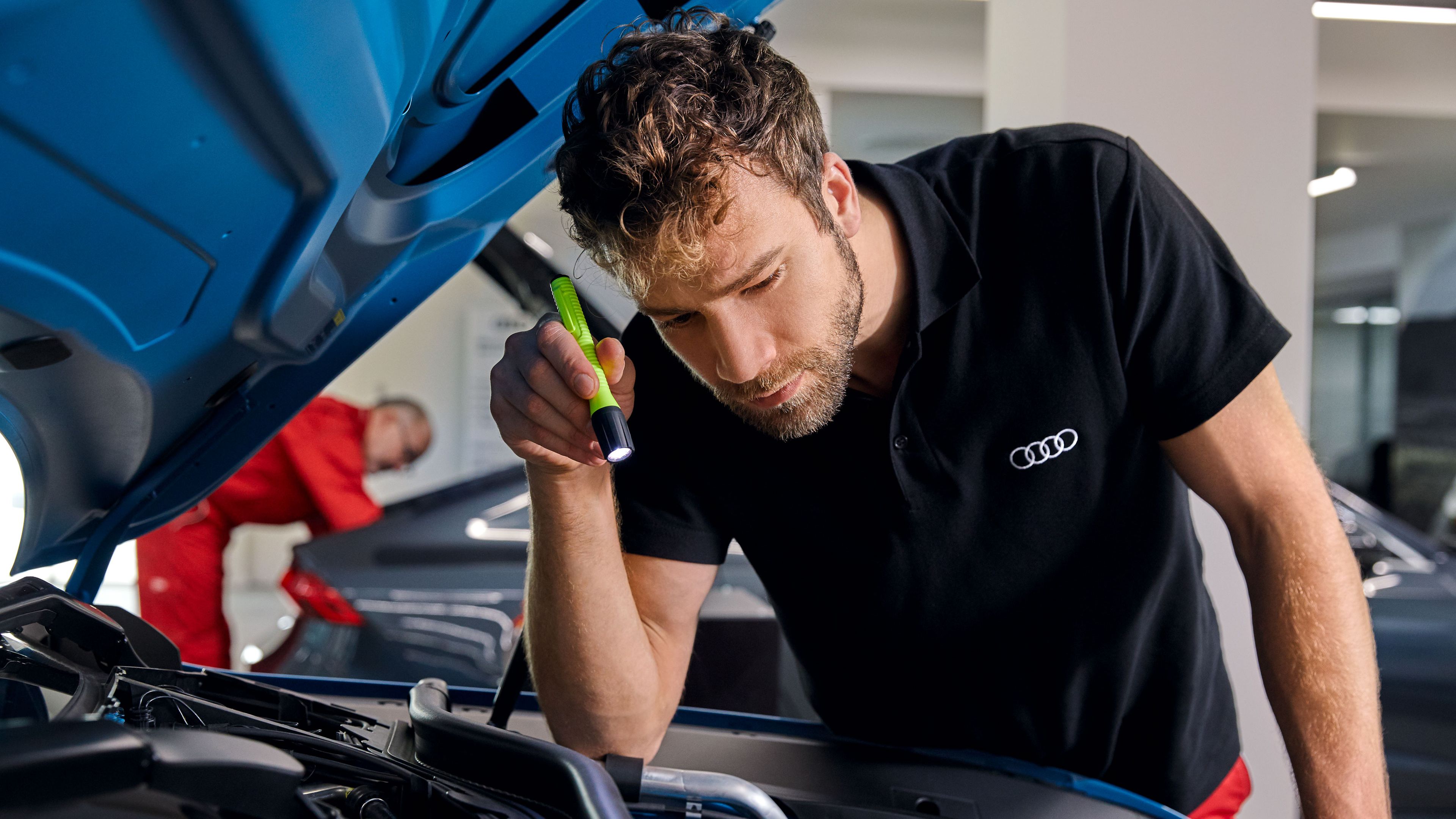 Ein Audi Service Techniker leuchtet mit einer Taschenlampe in den Motorraum eines Audi