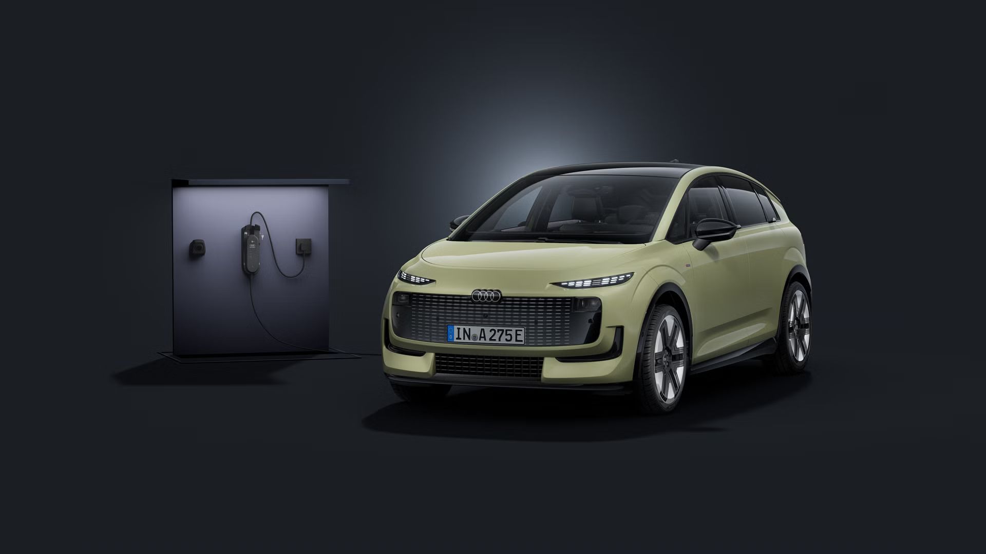Der Audi A2 e-tron schräg von vorn auf dunklem Hintergrund, links dahinter eine Ladesäule.