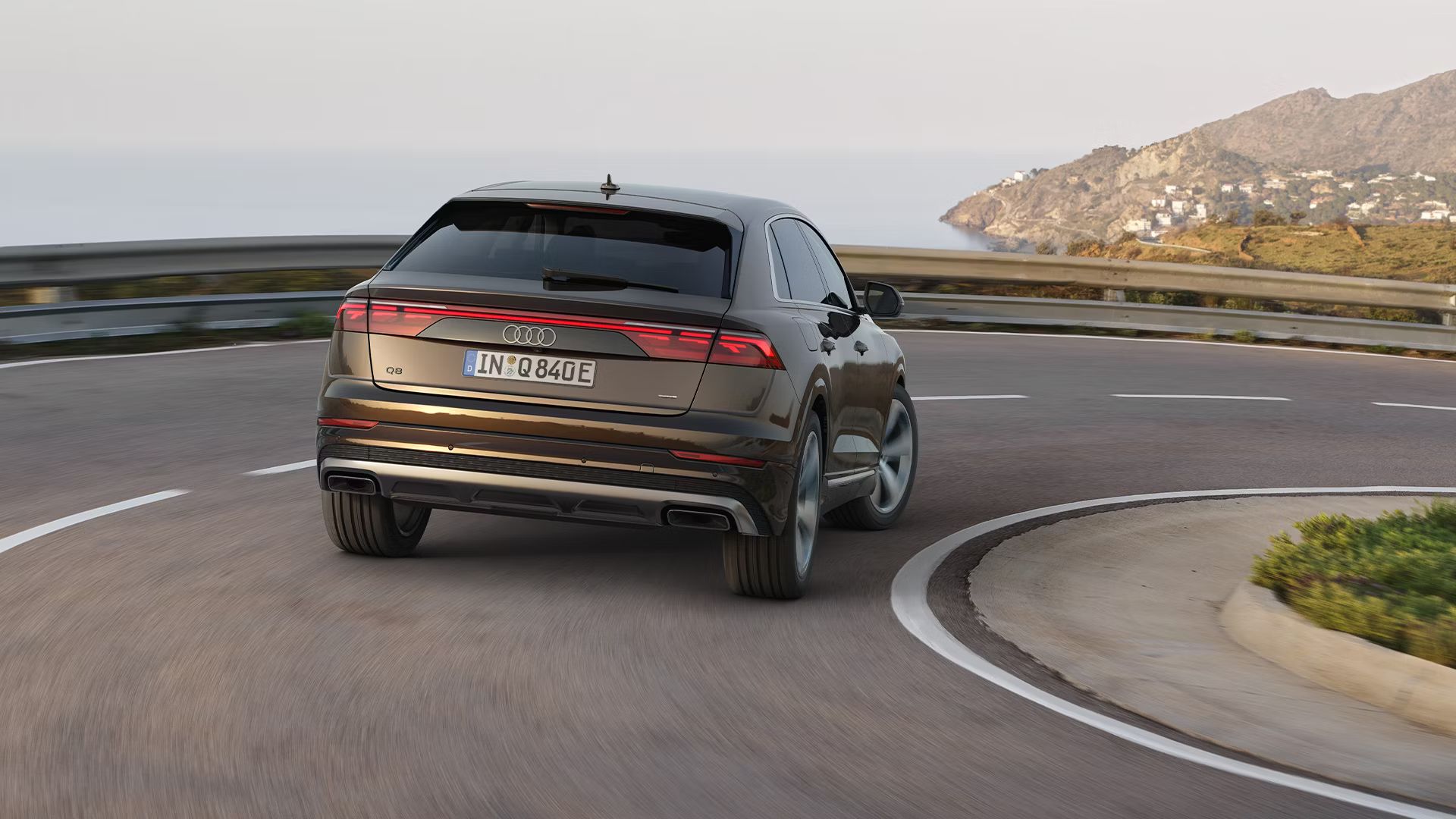 Audi Q8 в заден изглед, в движение по крайбрежен път със завой