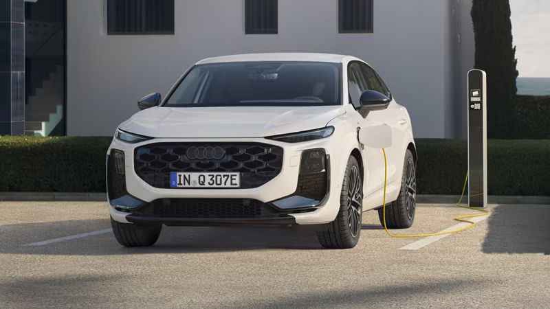 Auf dem Bild ist der Audi Q3 Sportback e-hybrid zu sehen. Dieser steht vor einem Wohngebäude mit einer Ladesäule und lädt.