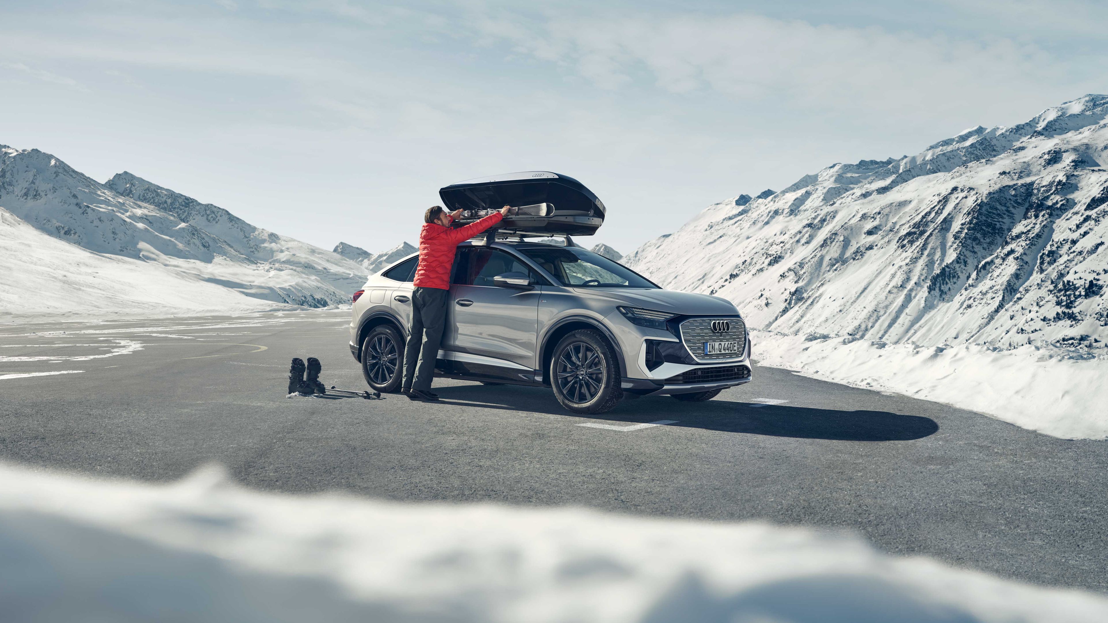 Ein Mann lädt seine Ski in eine Audi Dachbox die auf einem Audi Q4 montiert ist